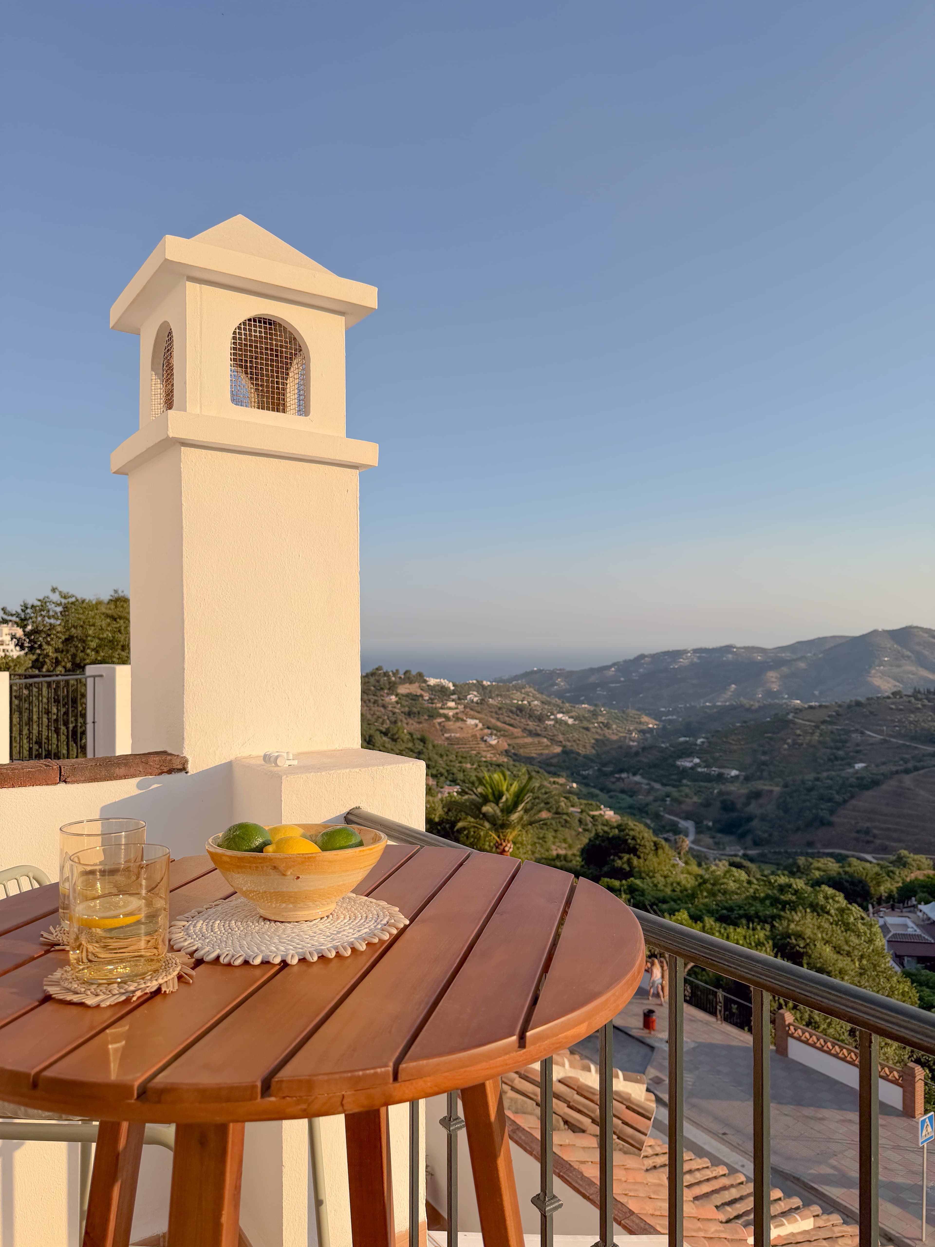 Terrace table with a bowl of lemons and limes, glasses of lemon water, and sea views past the chimney