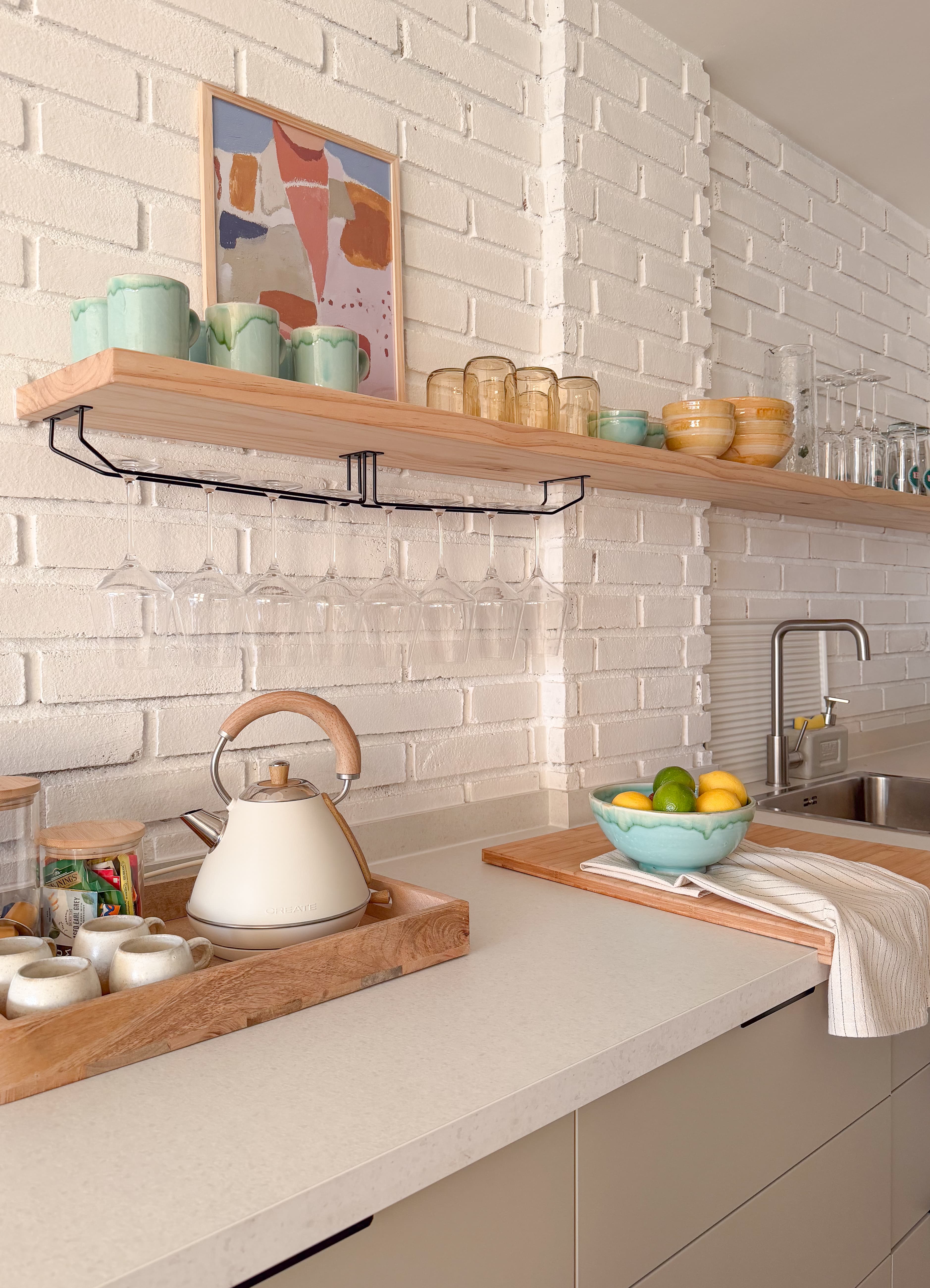 Kitchen open shelving with mint mugs, glassware, and a bowl of lemons and limes on the counter below