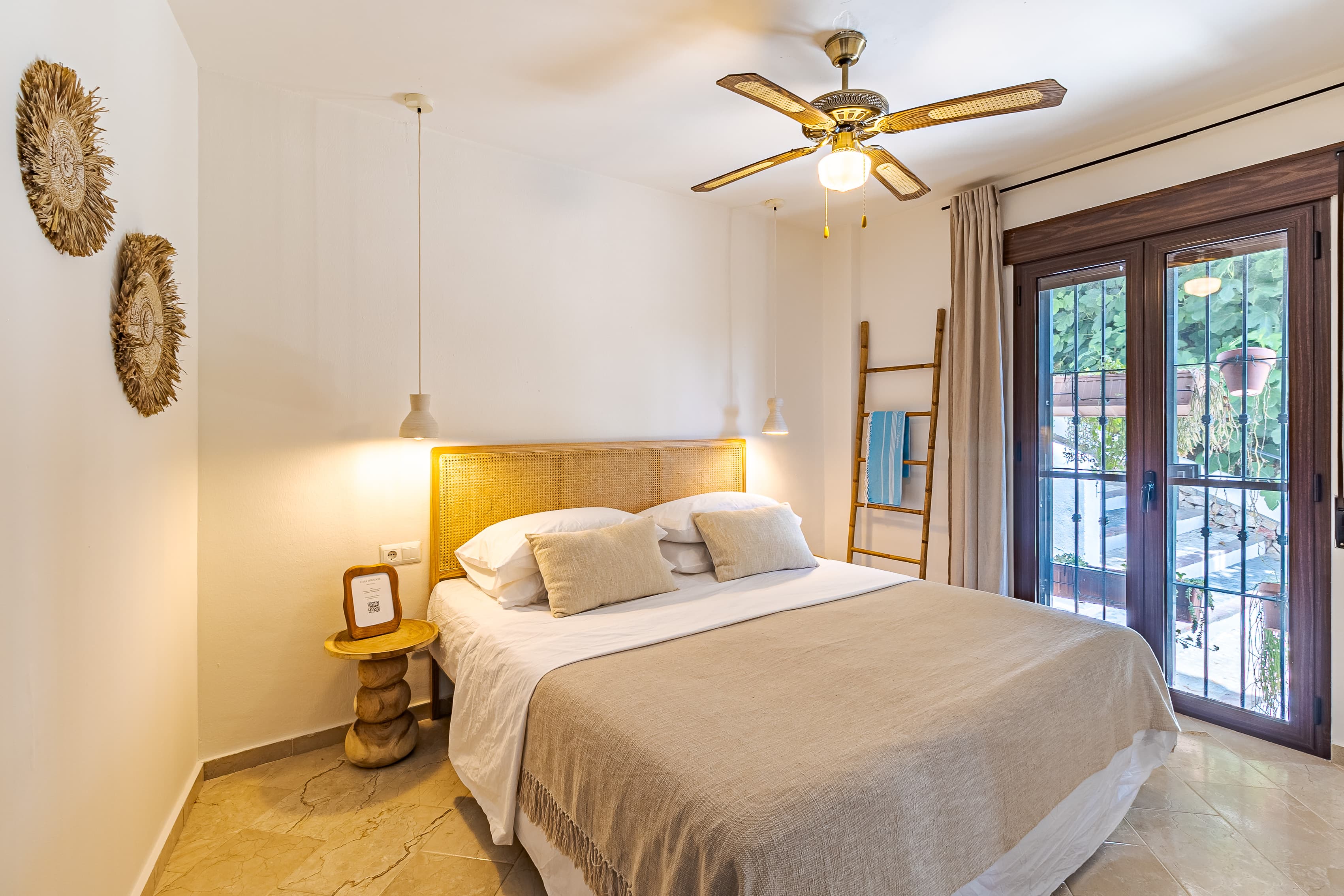 Master bedroom wide view with straw wall discs, a cane headboard, and French doors to the terrace
