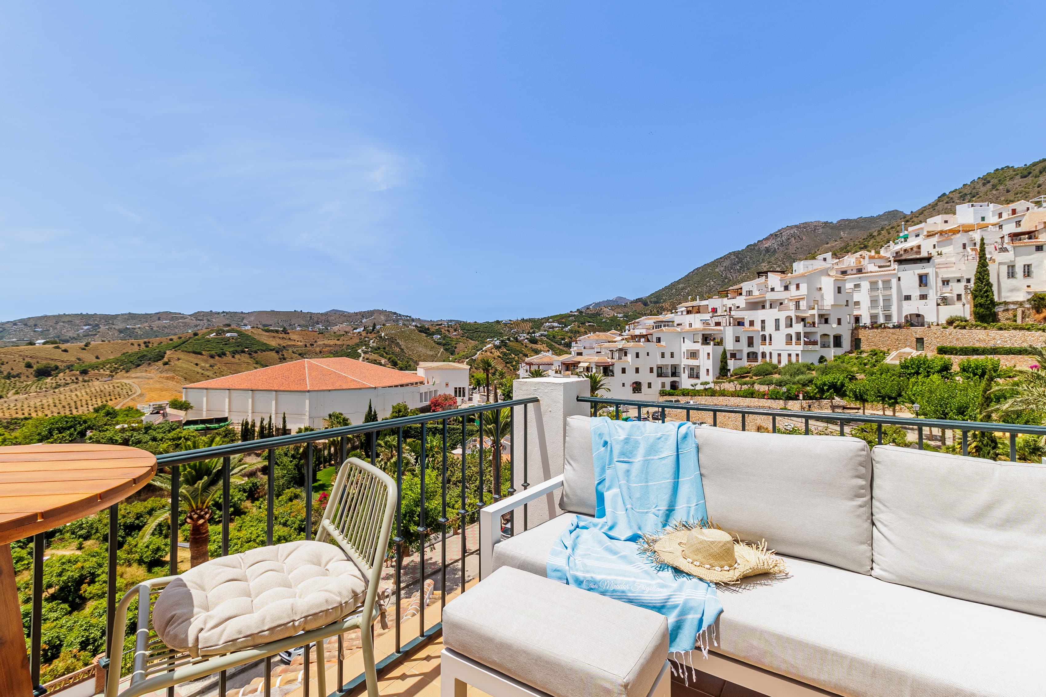 Terrace sofa with a blue throw and straw hat, overlooking the village and hills toward the sea